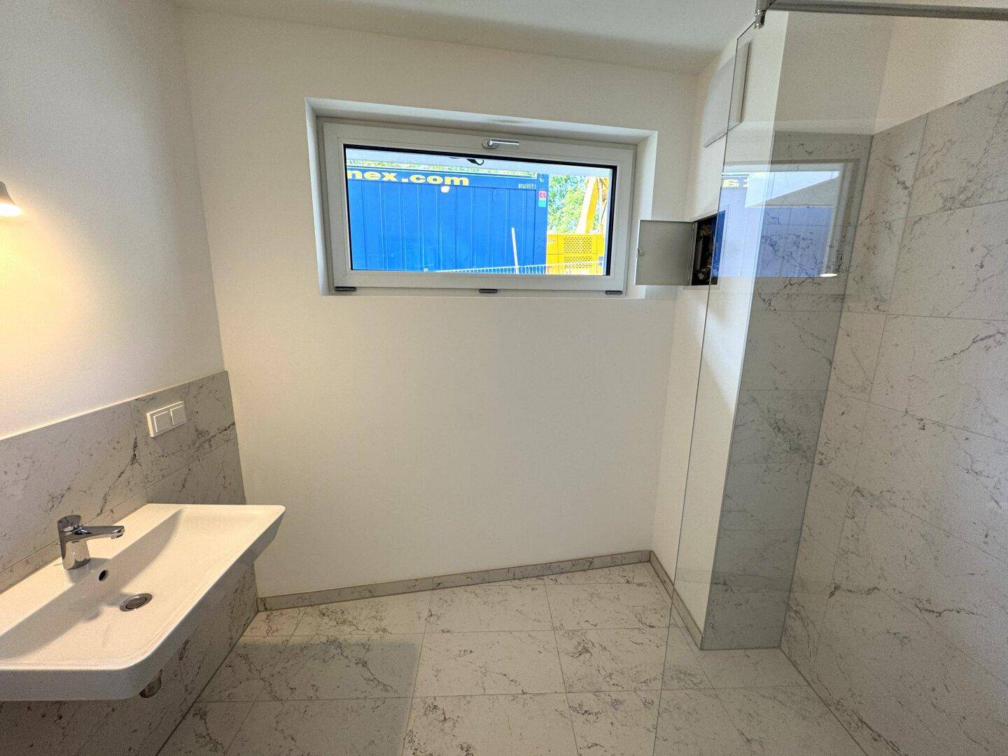 Helles Badezimmer mit modernem Waschbecken, großer Dusche und Fenster für natürliche Belüftung.
