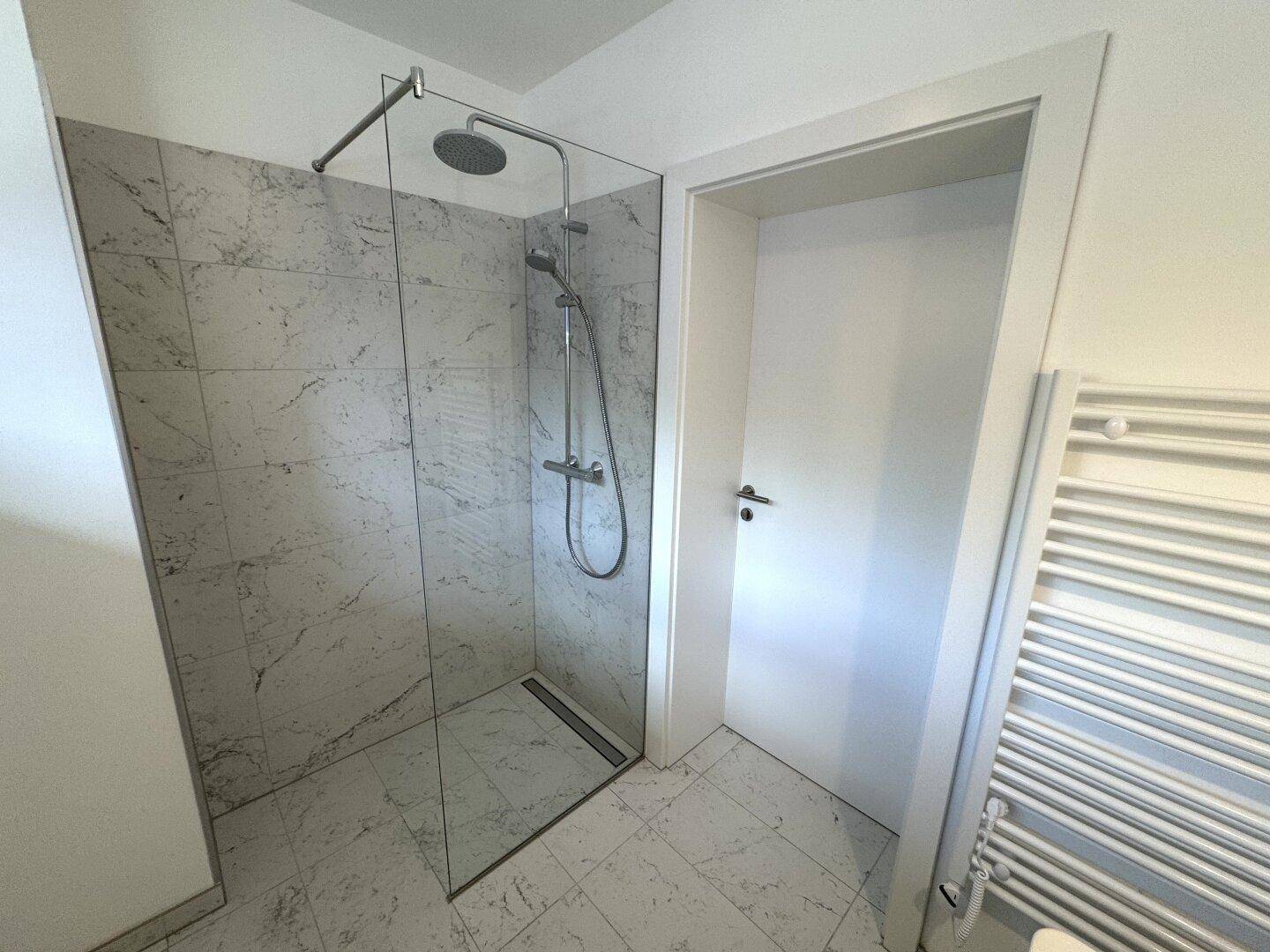 Modernes Badezimmer mit begehbarer Dusche, eleganten Marmorfliesen und beheiztem Handtuchhalter.