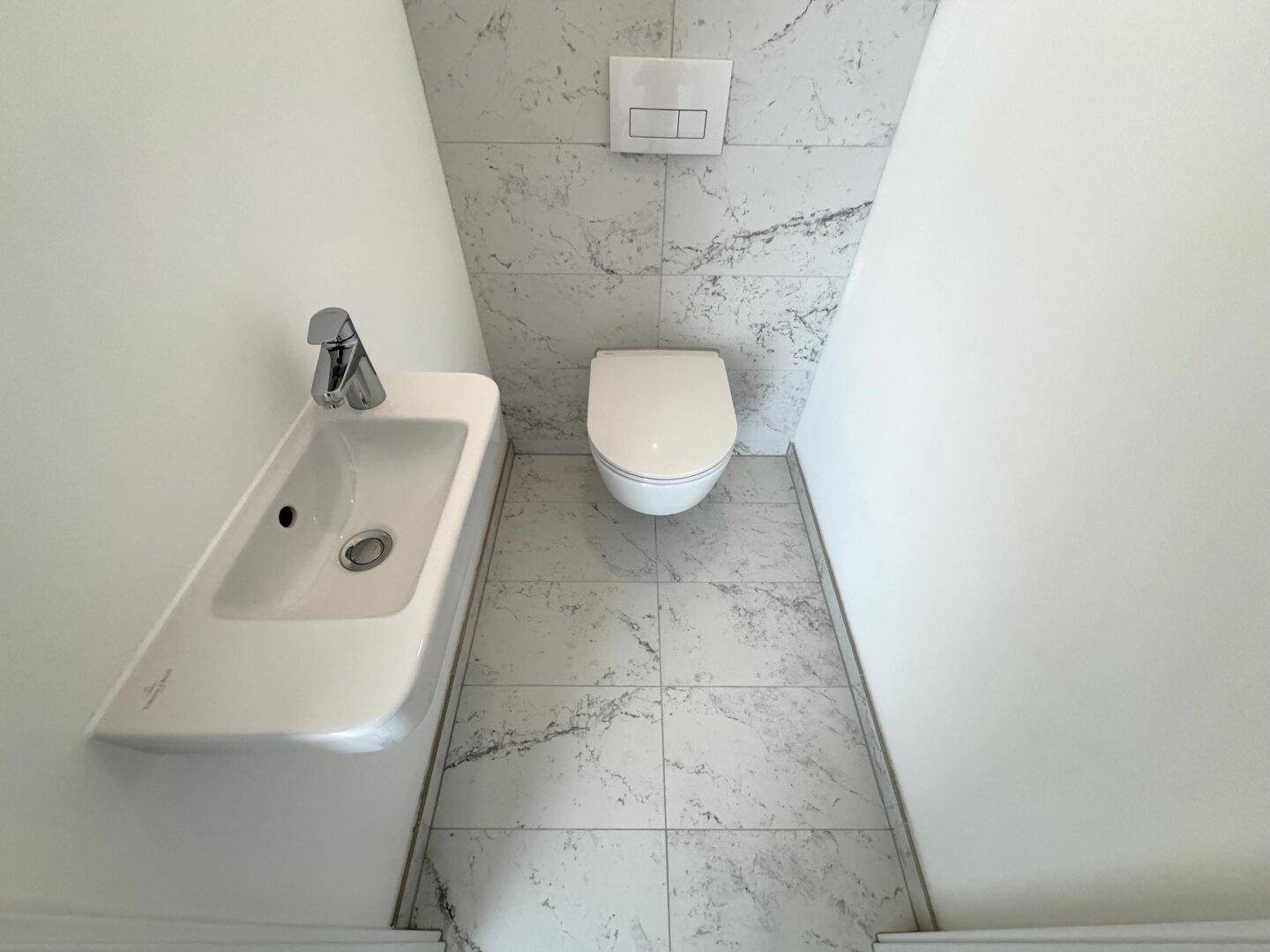 Kompaktes Gäste-WC mit Wand-WC, kleinem Waschbecken und modernen Marmorfliesen.