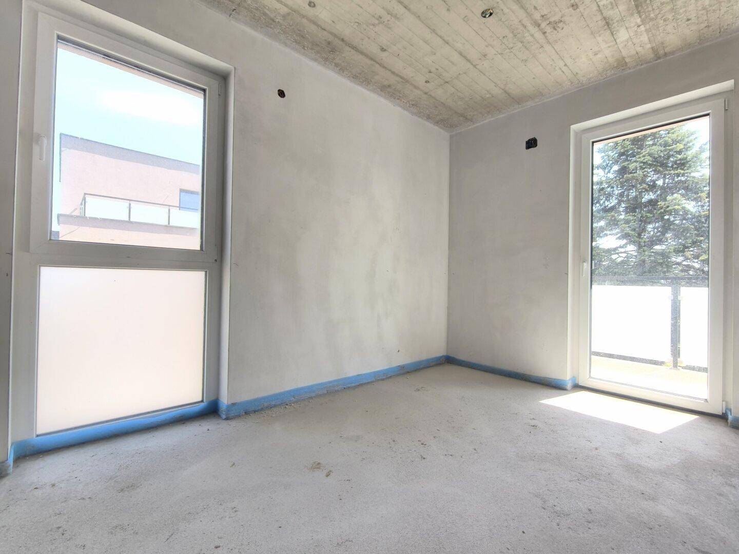Heller Rohbau-Raum mit zwei Fenstern und Betonboden, ideal für individuelle Gestaltung.