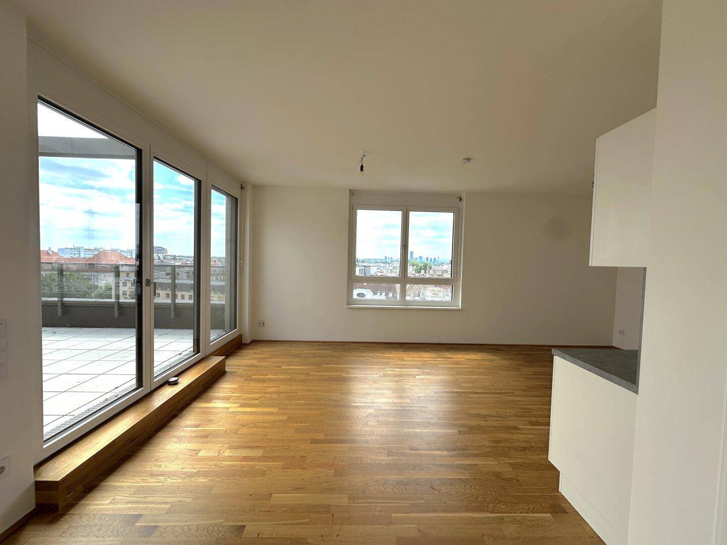Geräumiger Wohnbereich mit Zugang zur Terrasse, großen Glasfronten und hellem Parkettboden.