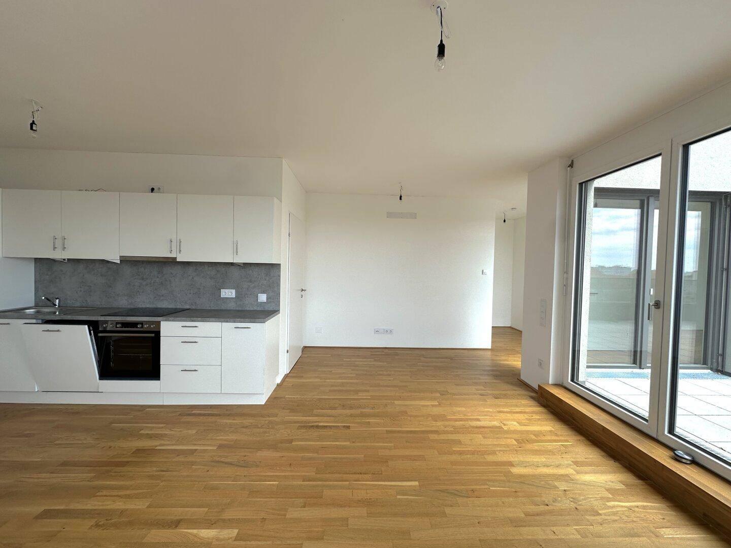 Offener Wohnbereich mit moderner Küchenzeile, Holzboden und direktem Zugang zur sonnigen Terrasse.
