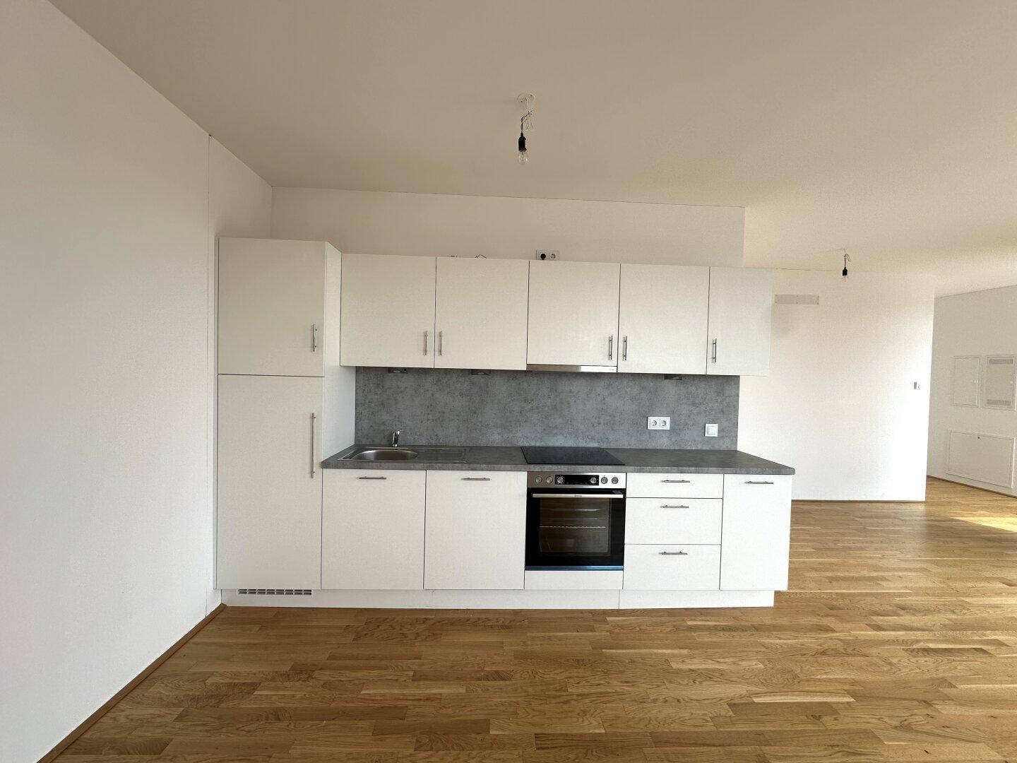 Moderne Einbauküche mit weißen Schränken, integriertem Backofen und viel Stauraum in hellem Ambiente.