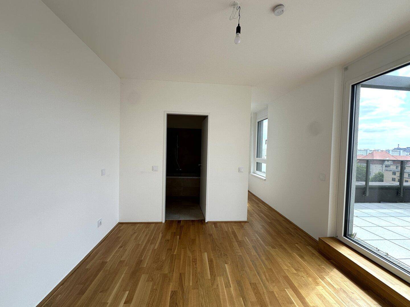 Helles Schlafzimmer mit Parkettboden und Zugang zu einem angrenzenden Badezimmer.