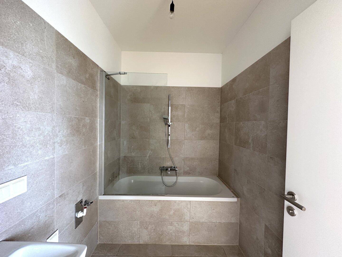 Modernes Badezimmer mit Badewanne, Duschabtrennung und beigefarbenen Fliesen an Wänden und Boden.