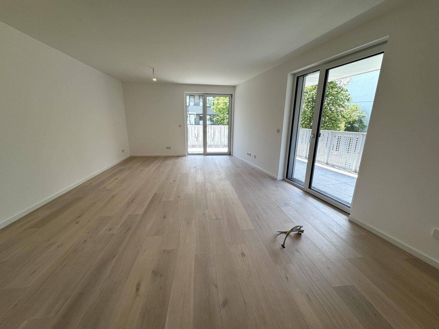 Geräumiges, helles Wohnzimmer mit hellem Holzparkett und großen Fenstern zum Balkon.