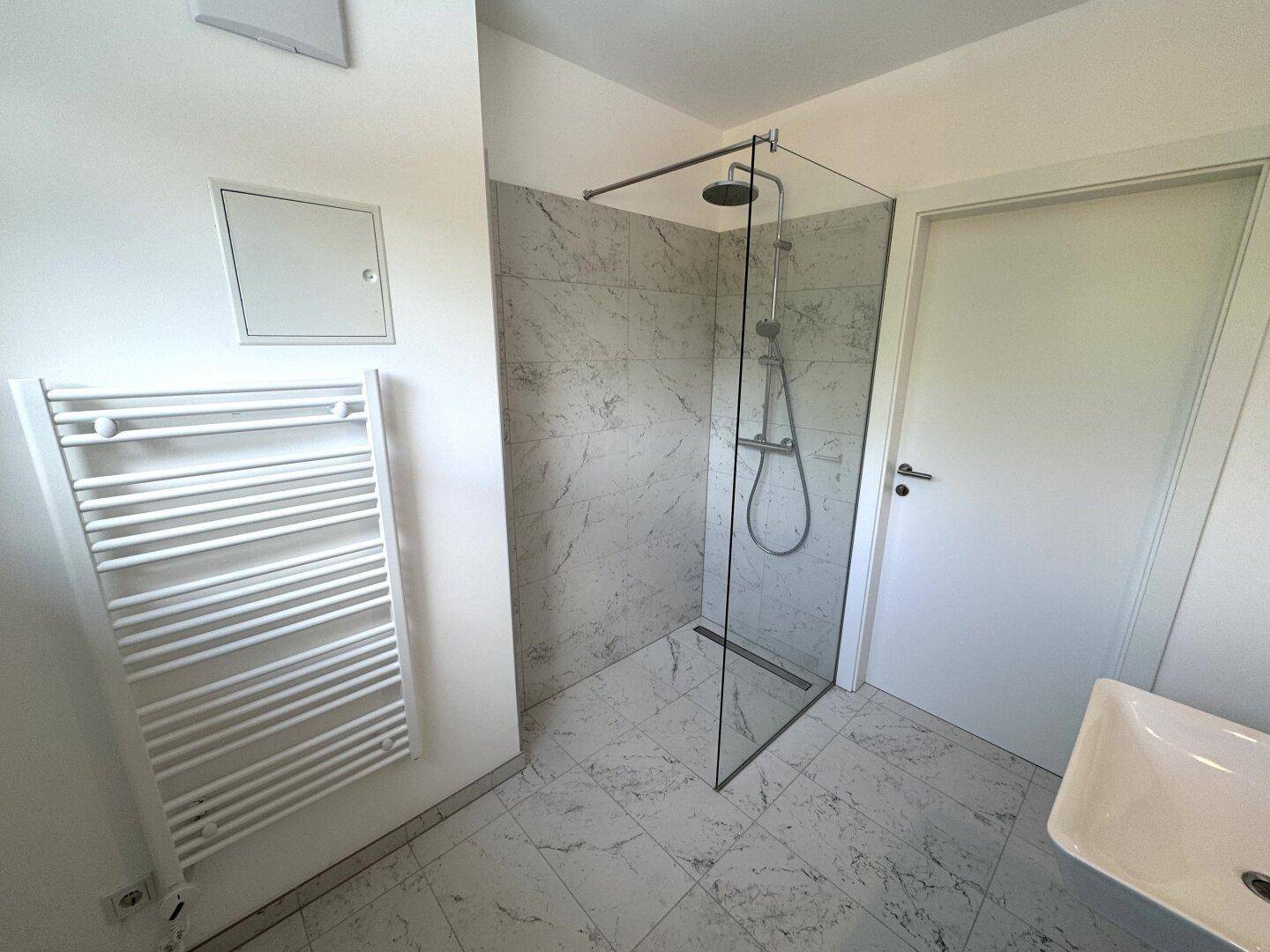 Modernes Badezimmer mit begehbarer Dusche, Fliesenboden und beheiztem Handtuchhalter.