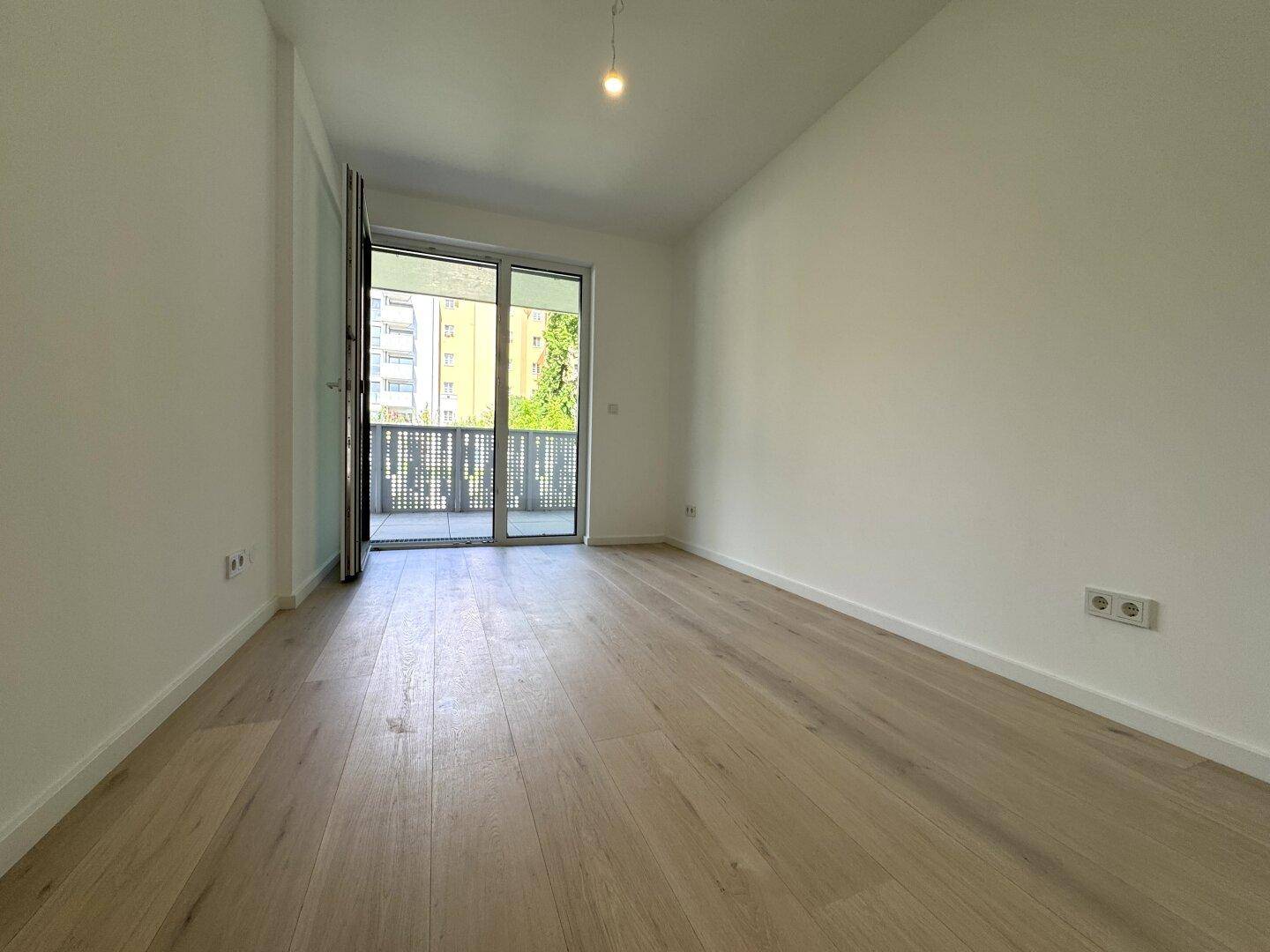 Heller, leerer Raum mit hellem Holzfußboden und Zugang zu einem Balkon.
