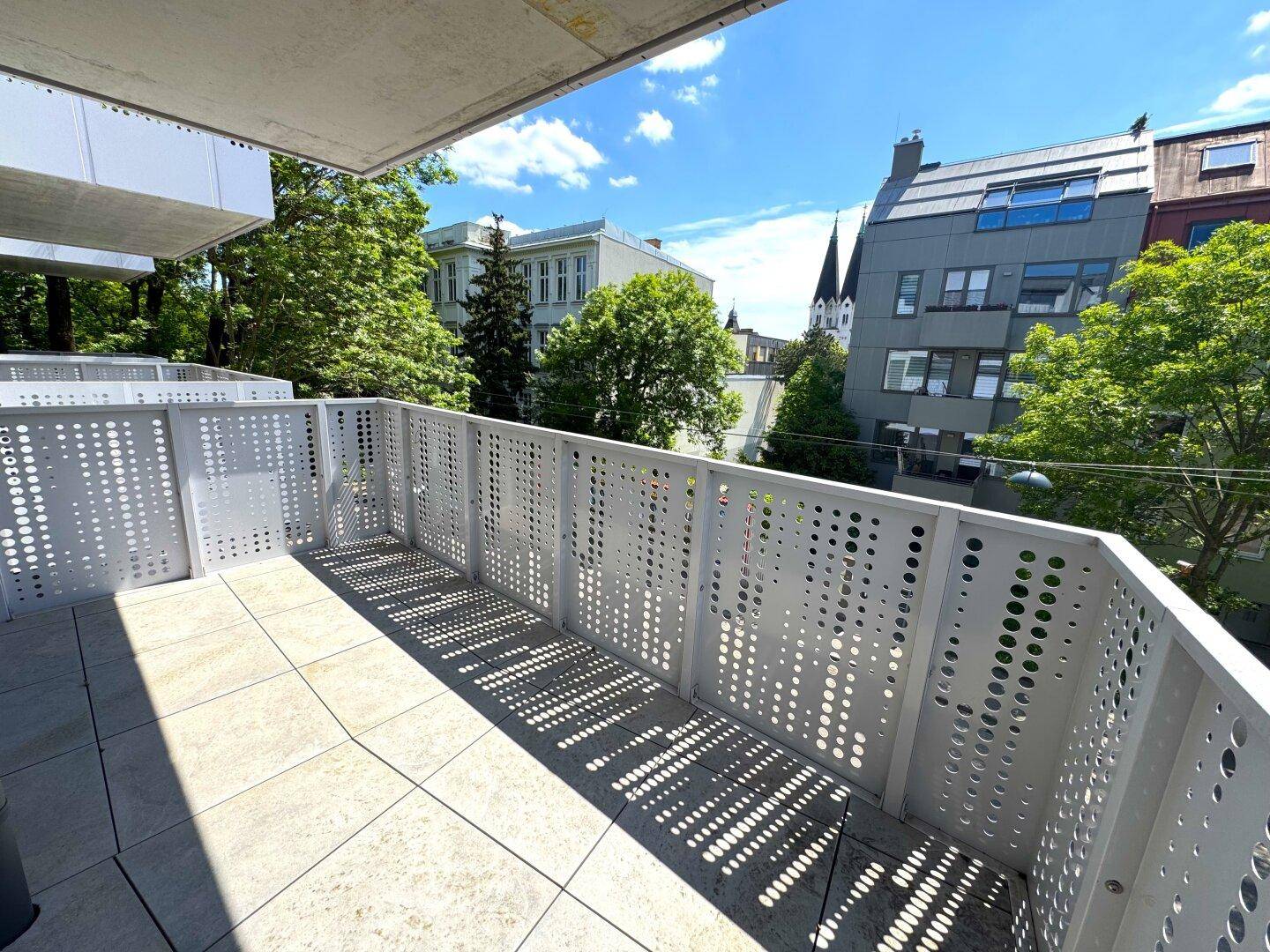 Heller Balkon mit modernen Lochblechgeländern und Fliesenboden, bietet einen Blick auf die Umgebung.