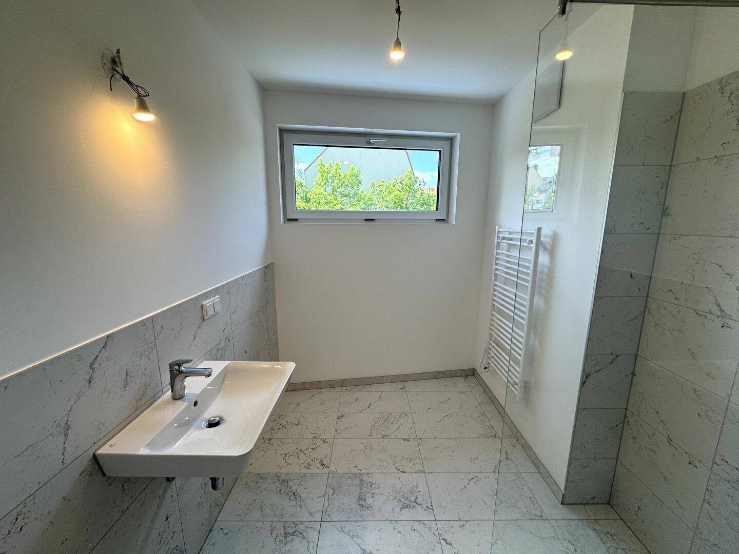 Modernes Badezimmer mit hellgrauen Fliesen, Einzelwaschbecken, Fenster und beheiztem Handtuchhalter.