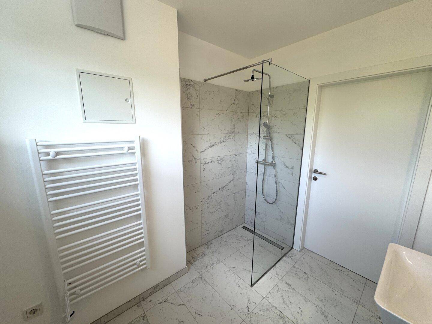 Modernes Badezimmer mit begehbarer Dusche, Glasabtrennung und beheiztem Handtuchhalter auf Fliesenboden.
