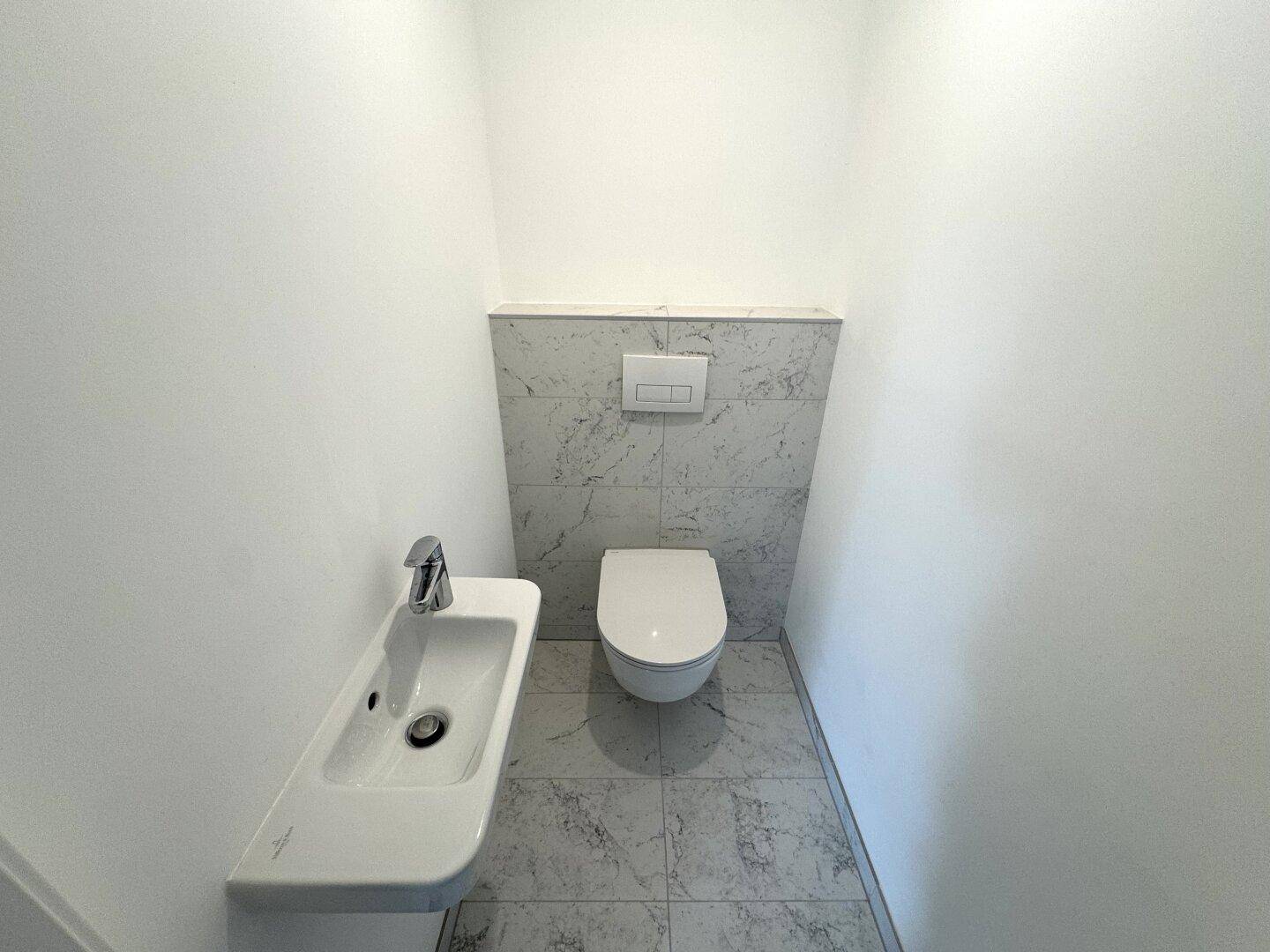Modernes Gäste-WC mit wandhängender Toilette, Einzelwaschbecken und hellgrauen Fliesen.
