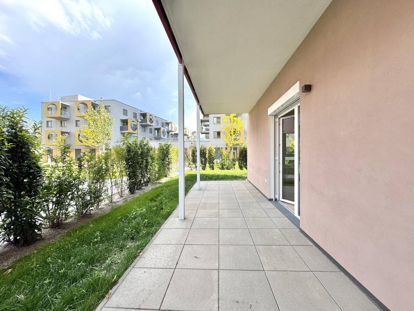 Ebenerdige Terrasse mit Fliesenboden und Blick auf eine grüne Hecke und moderne Gebäude.