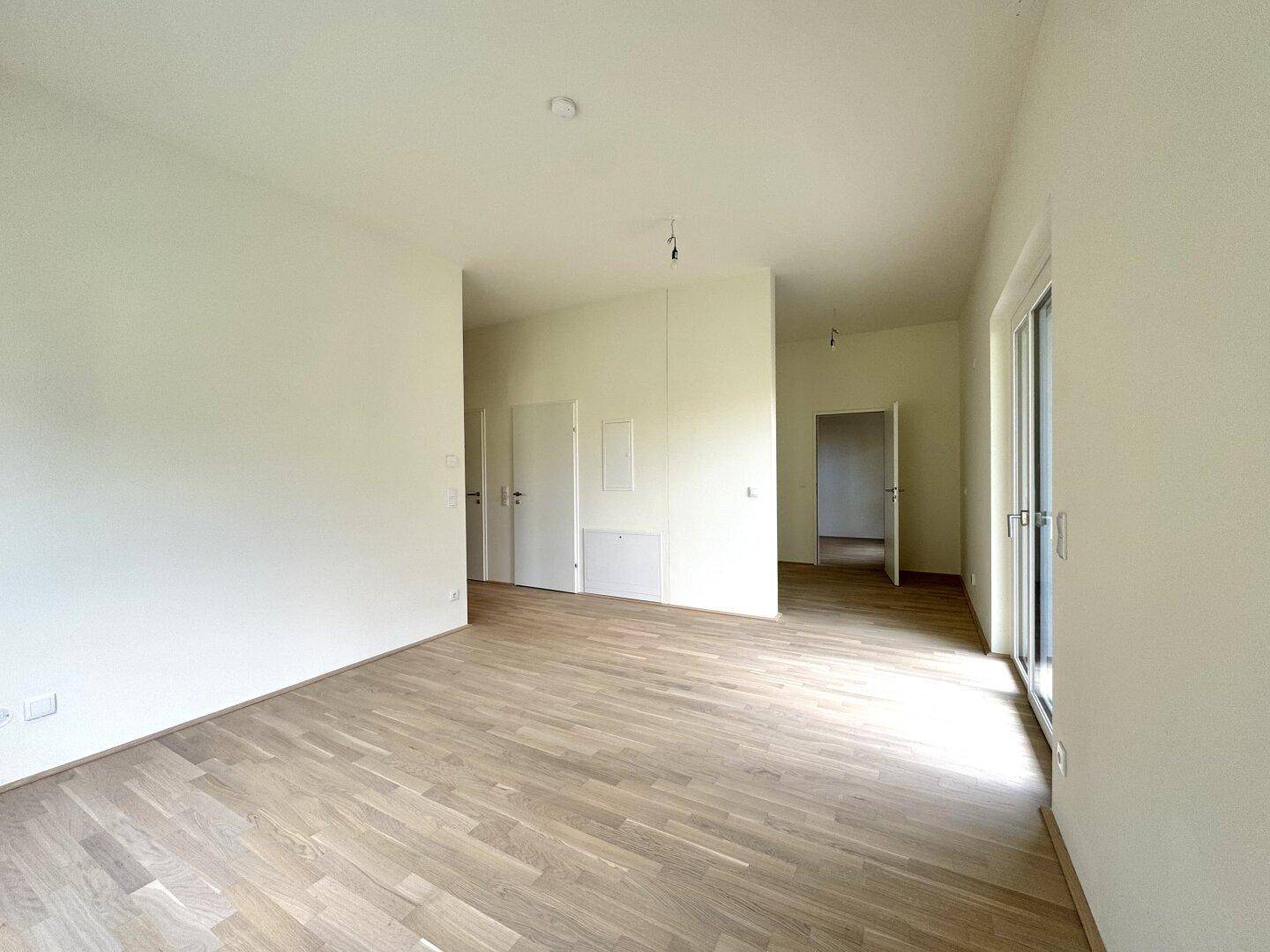 Heller, leerer Wohnraum mit hellem Laminatboden und weißen Wänden, bereit zum Einzug.