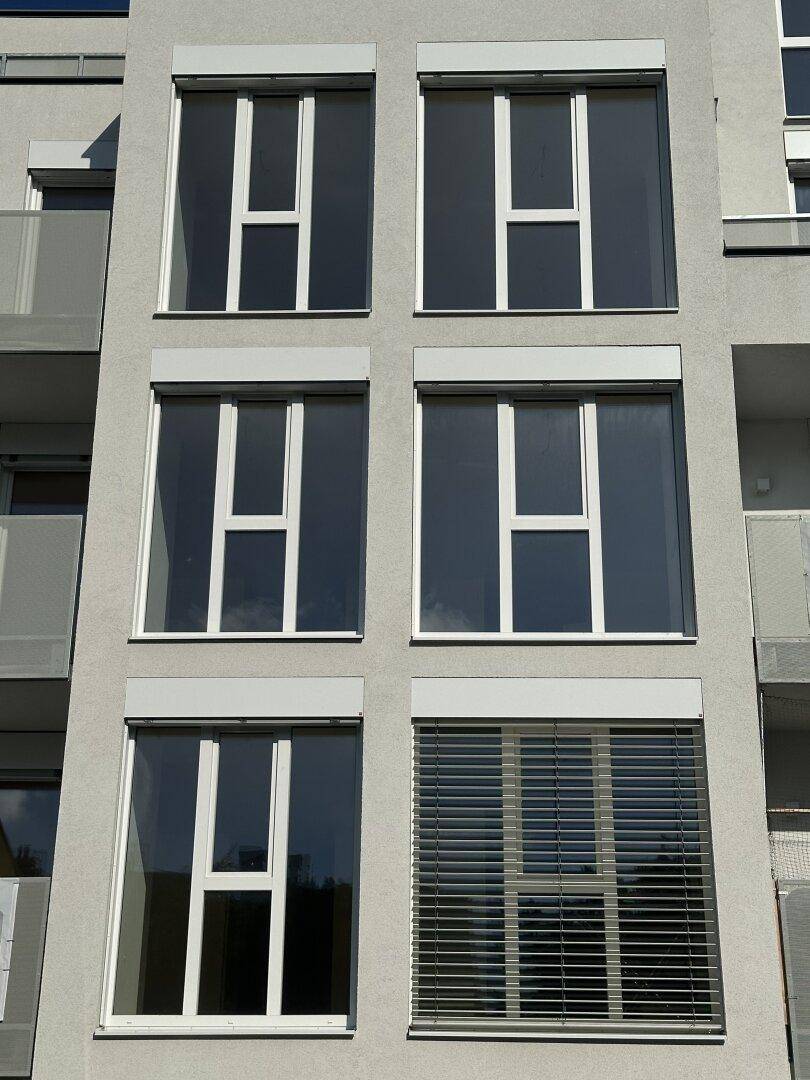 Detailansicht der Fensterfront mit modernen Rollläden und weißem Rahmen an der Gebäudefassade.