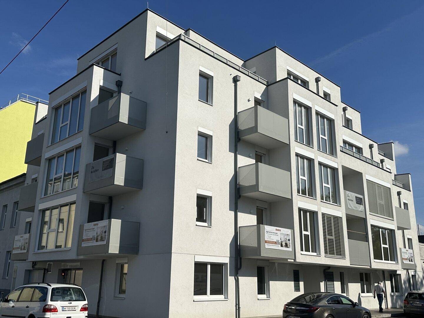 Modernes Mehrfamilienhaus mit Balkonen und großen Fenstern unter blauem Himmel.