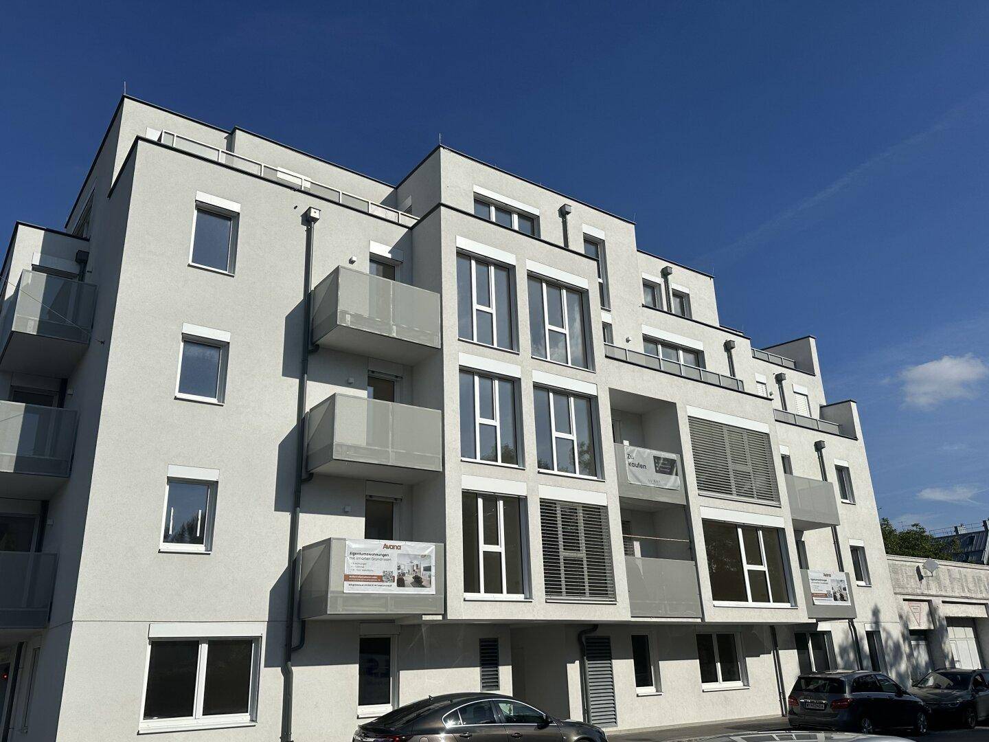 Ansicht eines modernen Wohngebäudes mit Balkonen und großen Fensterfronten bei sonnigem Wetter.