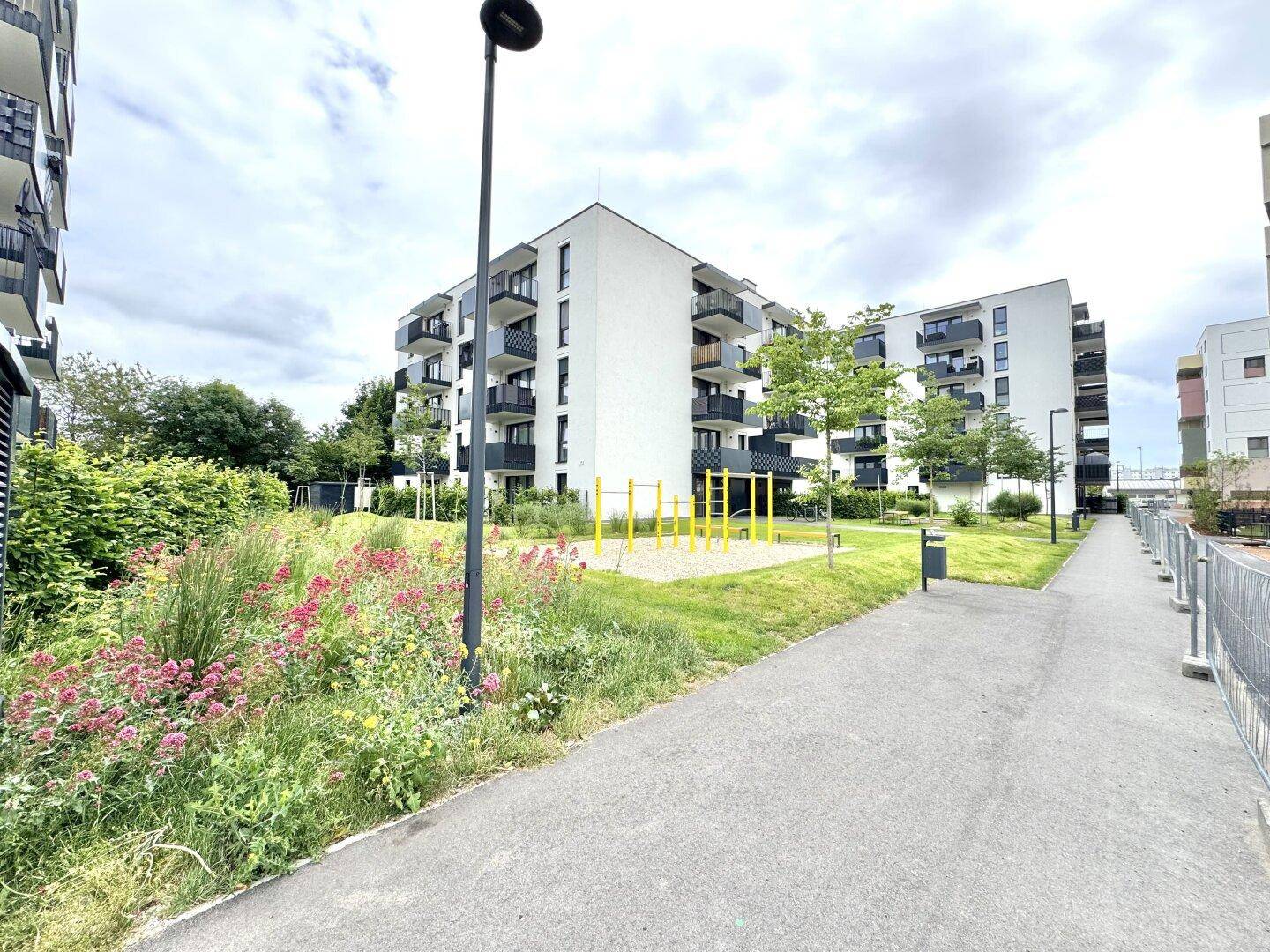 Moderne Wohngebäude mit Balkonen, umgeben von gepflegten Grünflächen und einem Spielplatz.