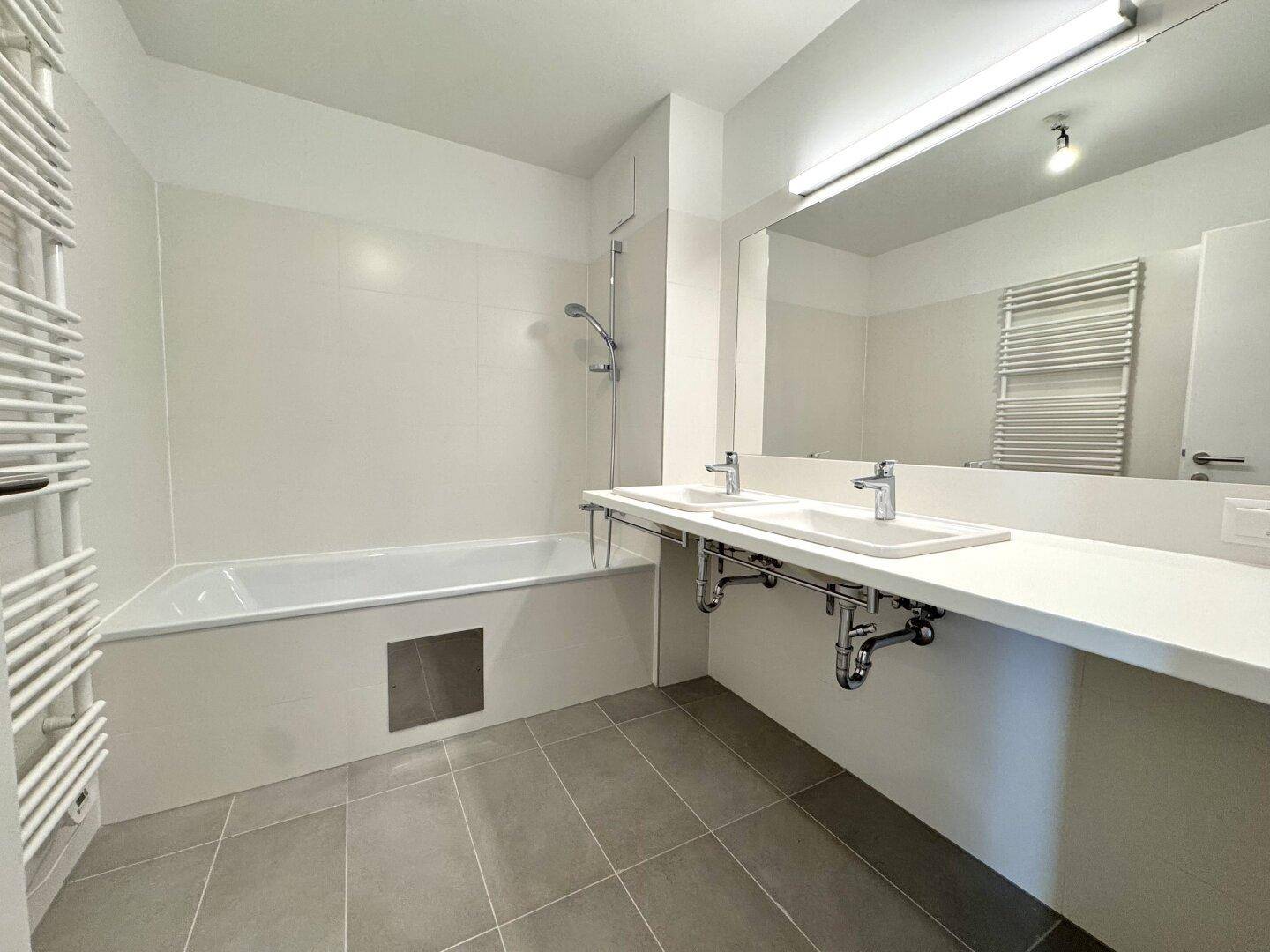 Modernes Badezimmer mit Badewanne, Doppelwaschbecken, großem Spiegel und Handtuchheizkörper.
