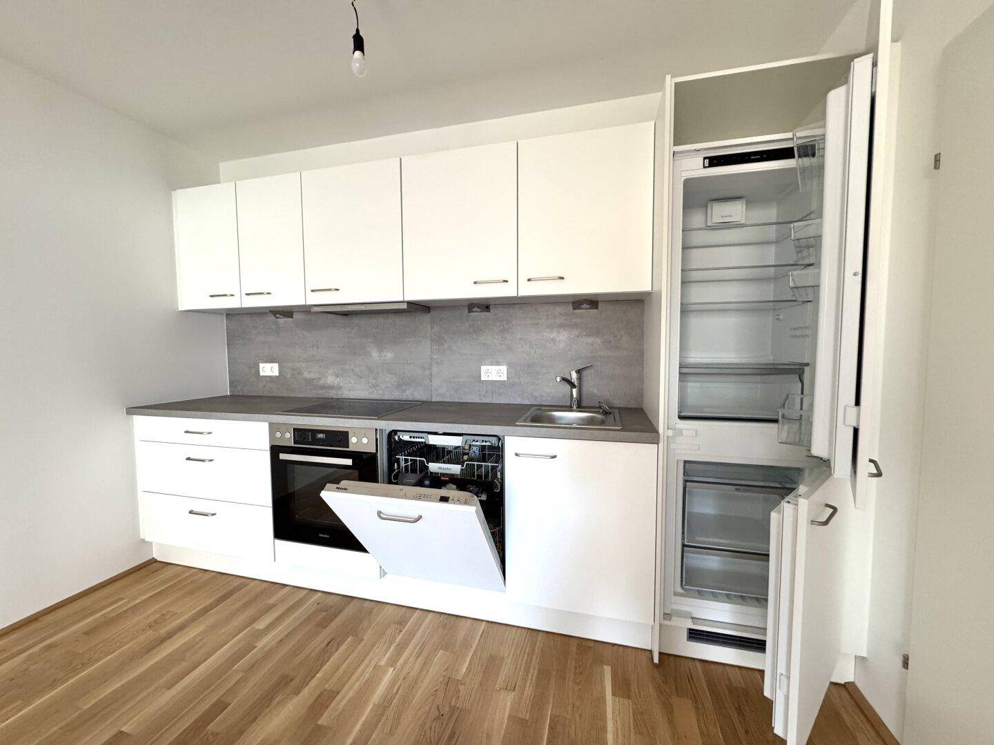 Moderne Einbauküche mit weißen Schränken, integrierten Geräten und hellem Parkettboden.