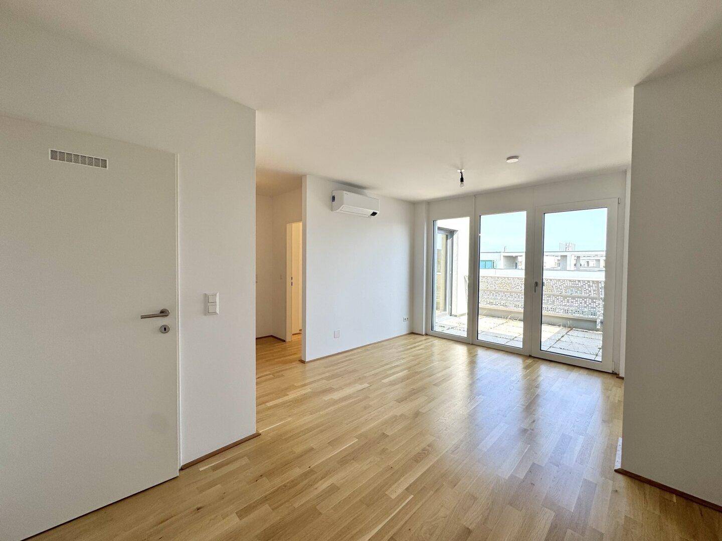 Helles Wohnzimmer mit Parkettboden, weißen Wänden, Klimaanlage und Zugang zur Terrasse.