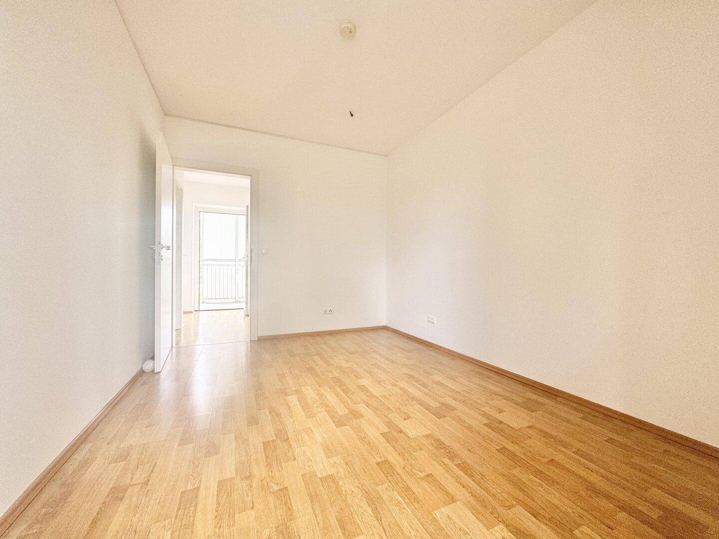 Leeres Zimmer mit Parkettboden und Zugang zu einem weiteren Raum.