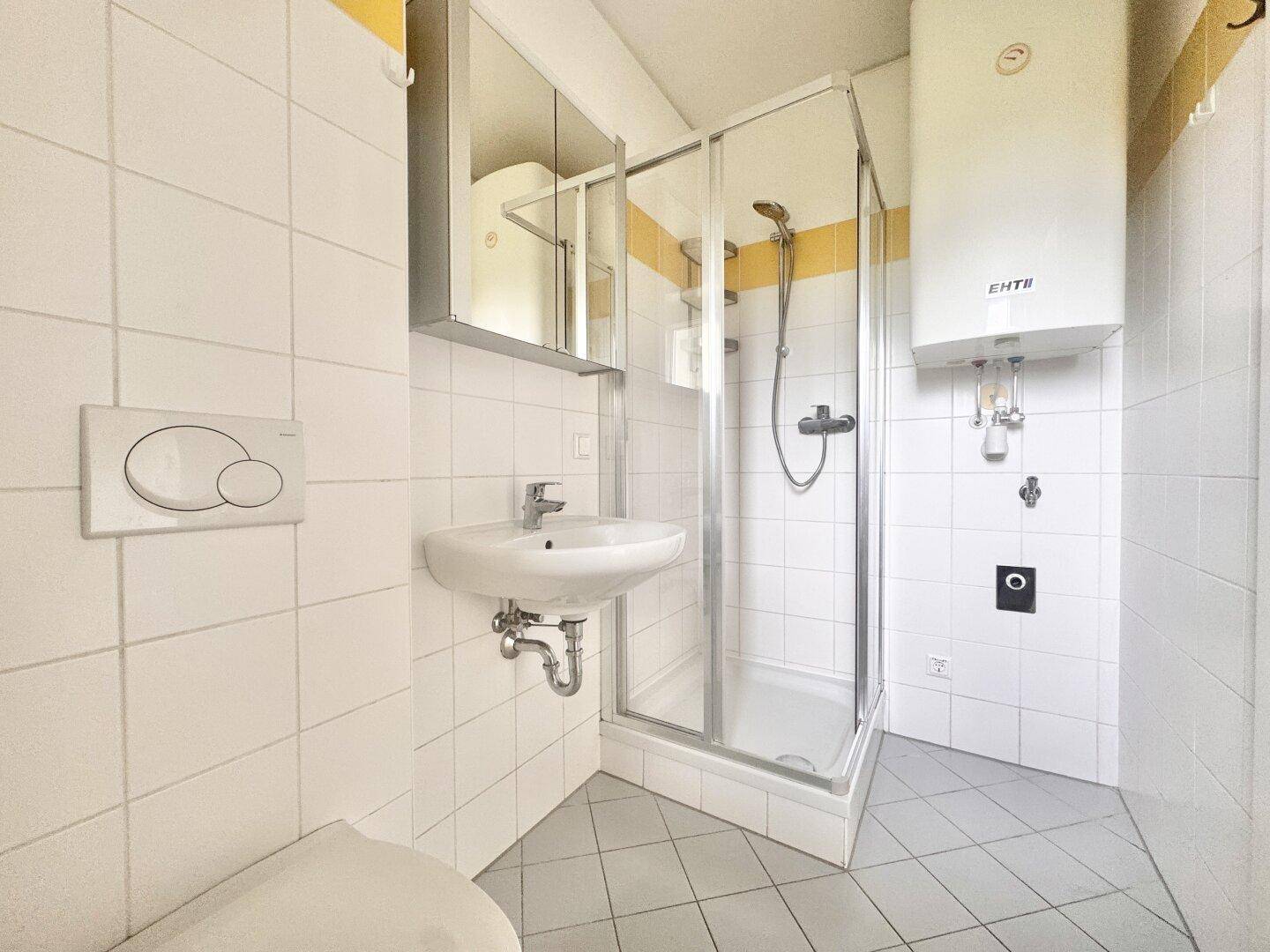 Gefliestes Badezimmer mit Dusche, Waschbecken und Toilette in hellem Design.