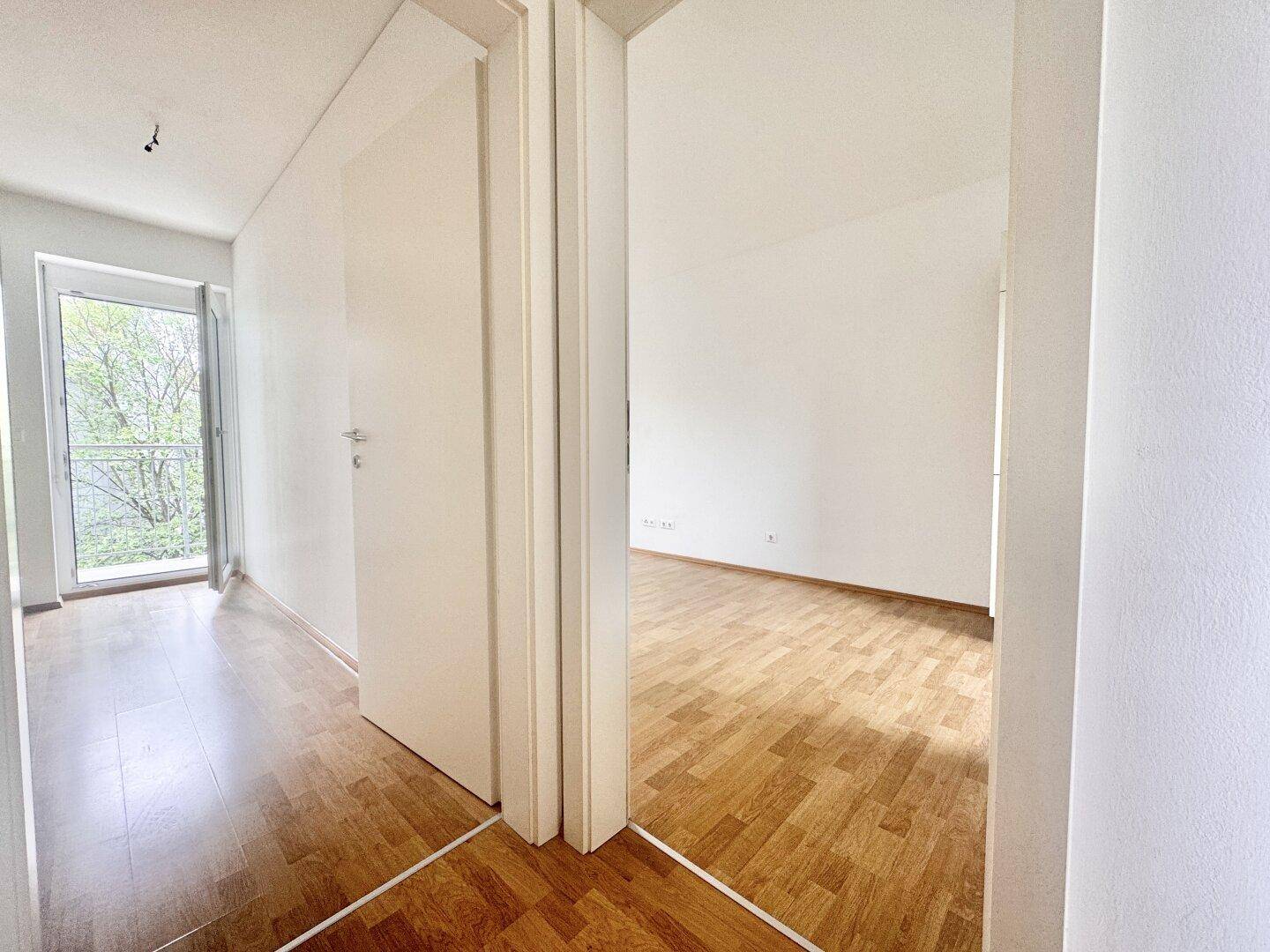 Heller Flur mit Parkettboden, der zu einem Zimmer mit Balkonzugang führt.