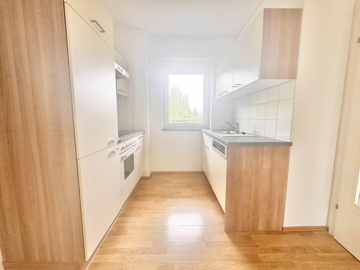 Funktionale Küche mit hellen Holzfronten, Einbaugeräten und Fenster.