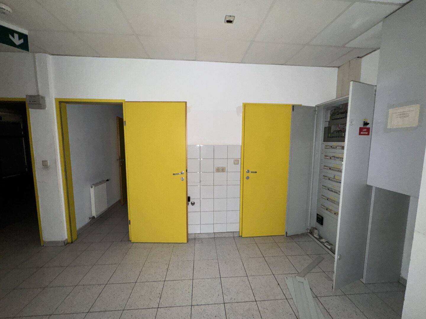 Flur mit zwei auffälligen gelben Türen, einem gefliesten Wandbereich und einem offenen Sicherungskasten.