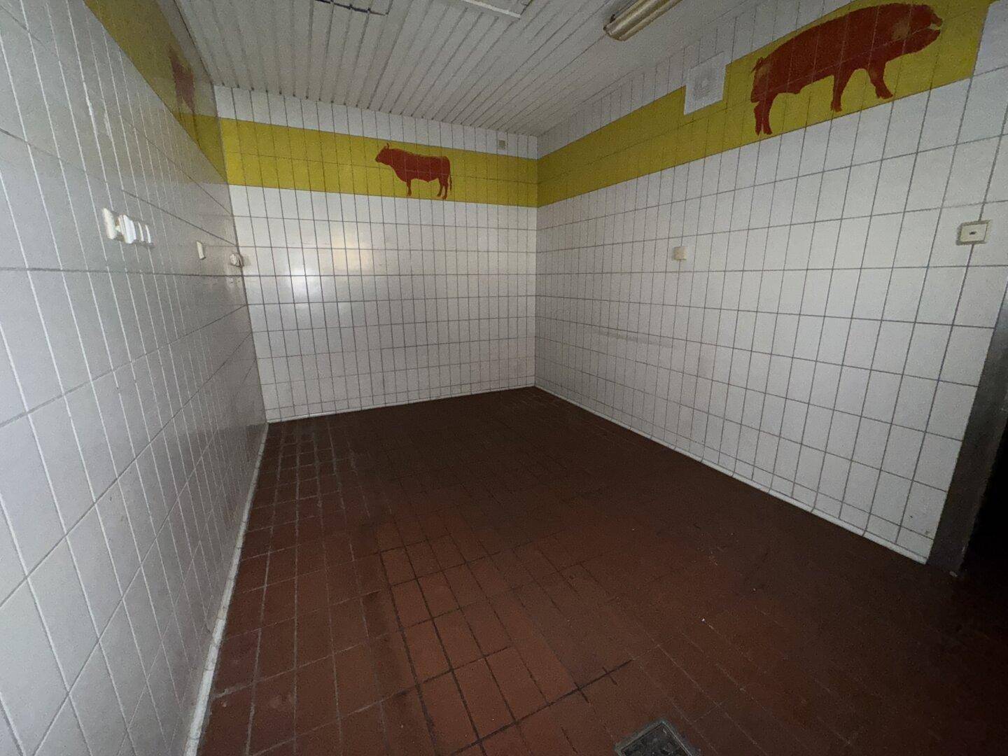 Gefliester Raum mit gelbem Streifen und Tier-Silhouetten, dunklem Boden, möglicherweise ein Kühlraum oder Vorbereitungsbereich.