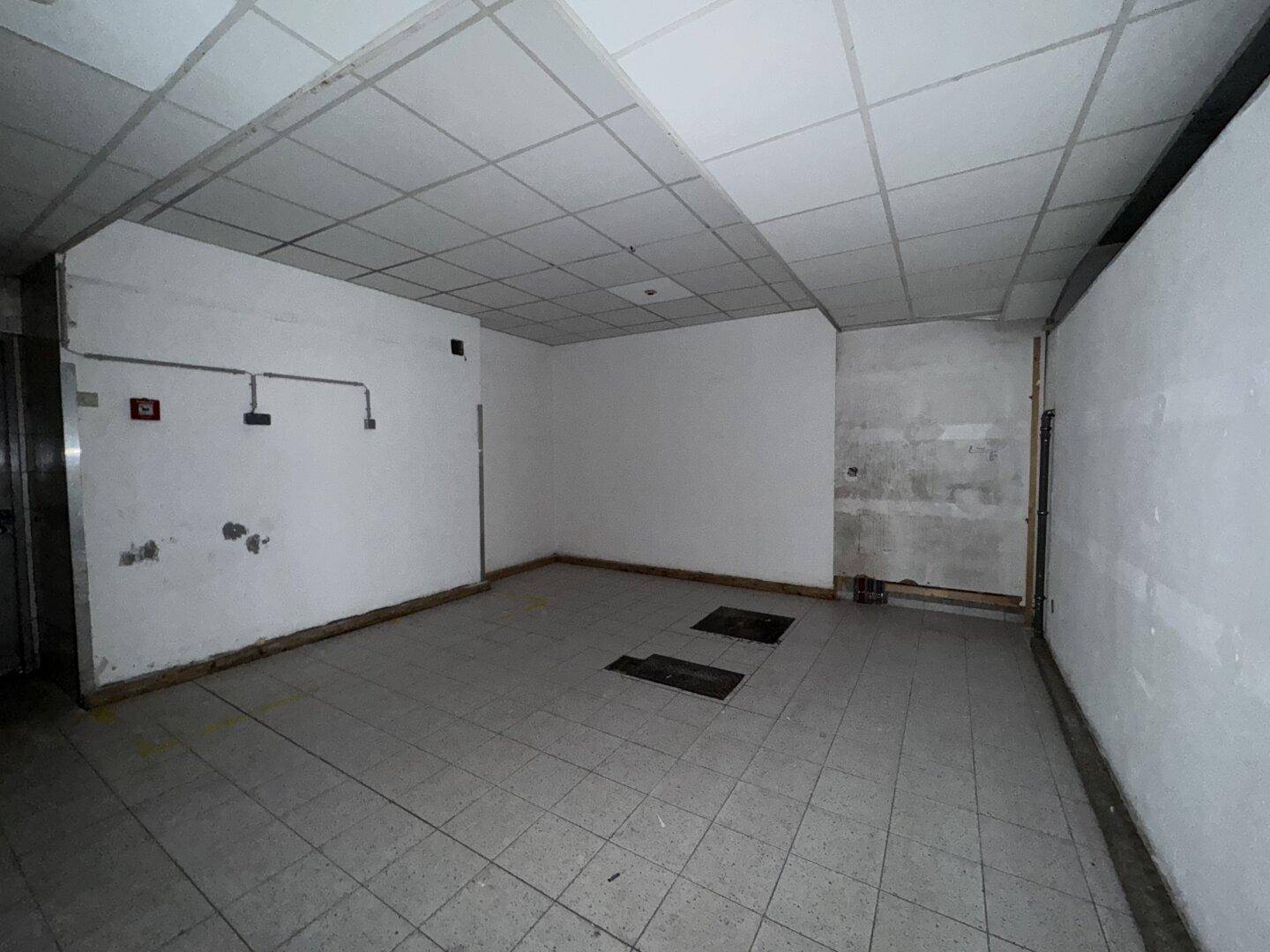 Leerer Lagerraum mit Fliesenboden, weißen Wänden und abgehängter Decke, bereit zur Nutzung.