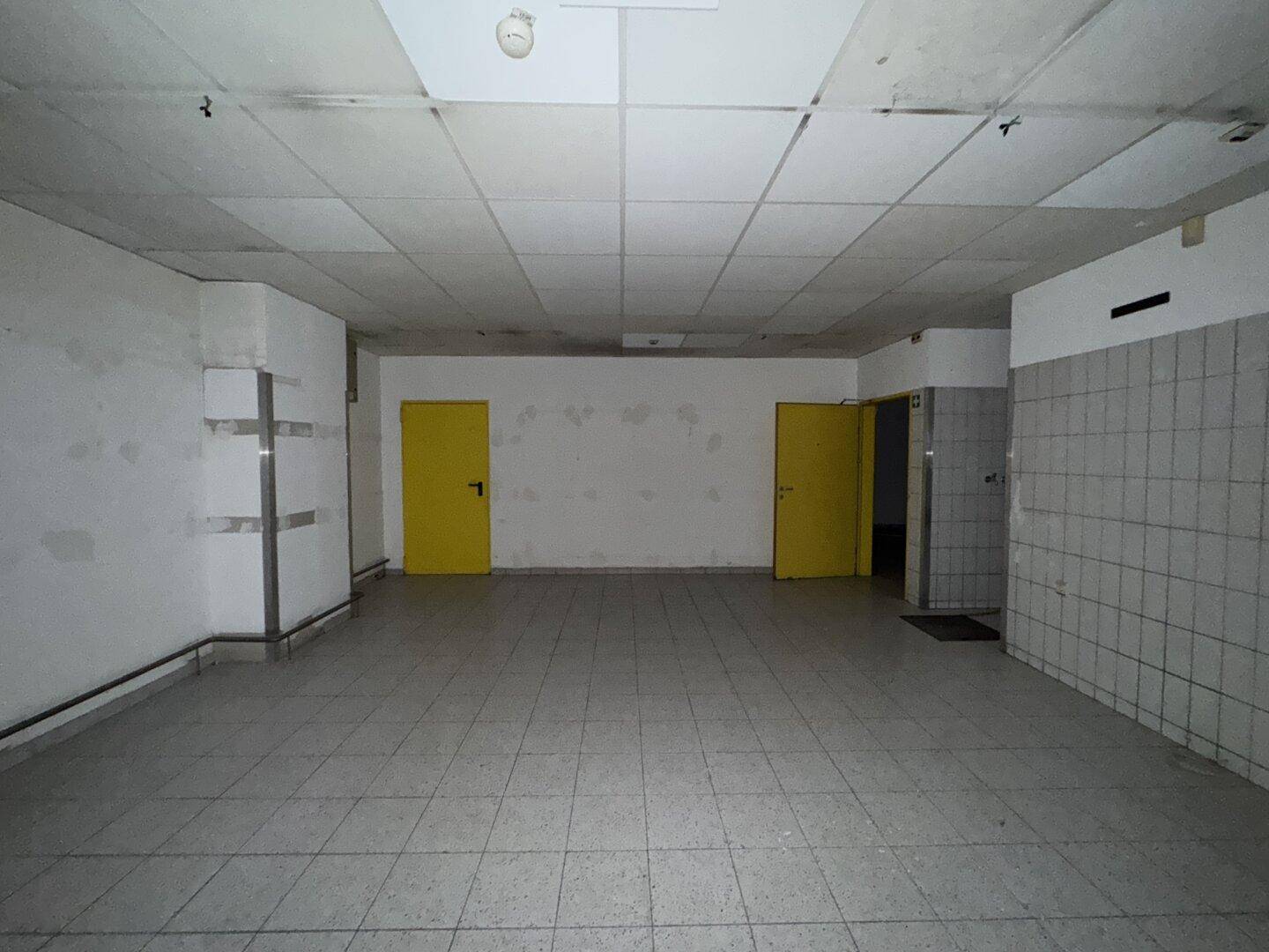 Raum mit Fliesenboden, weißen Wänden, zwei gelben Türen und einem gefliesten Bereich.