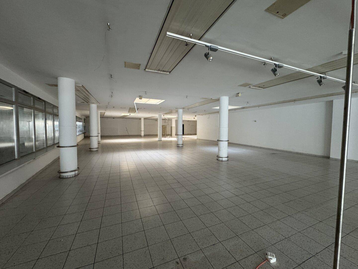Weitläufiger Gewerberaum mit vielen Säulen, großen Fenstern und Schienenbeleuchtung an der Decke.