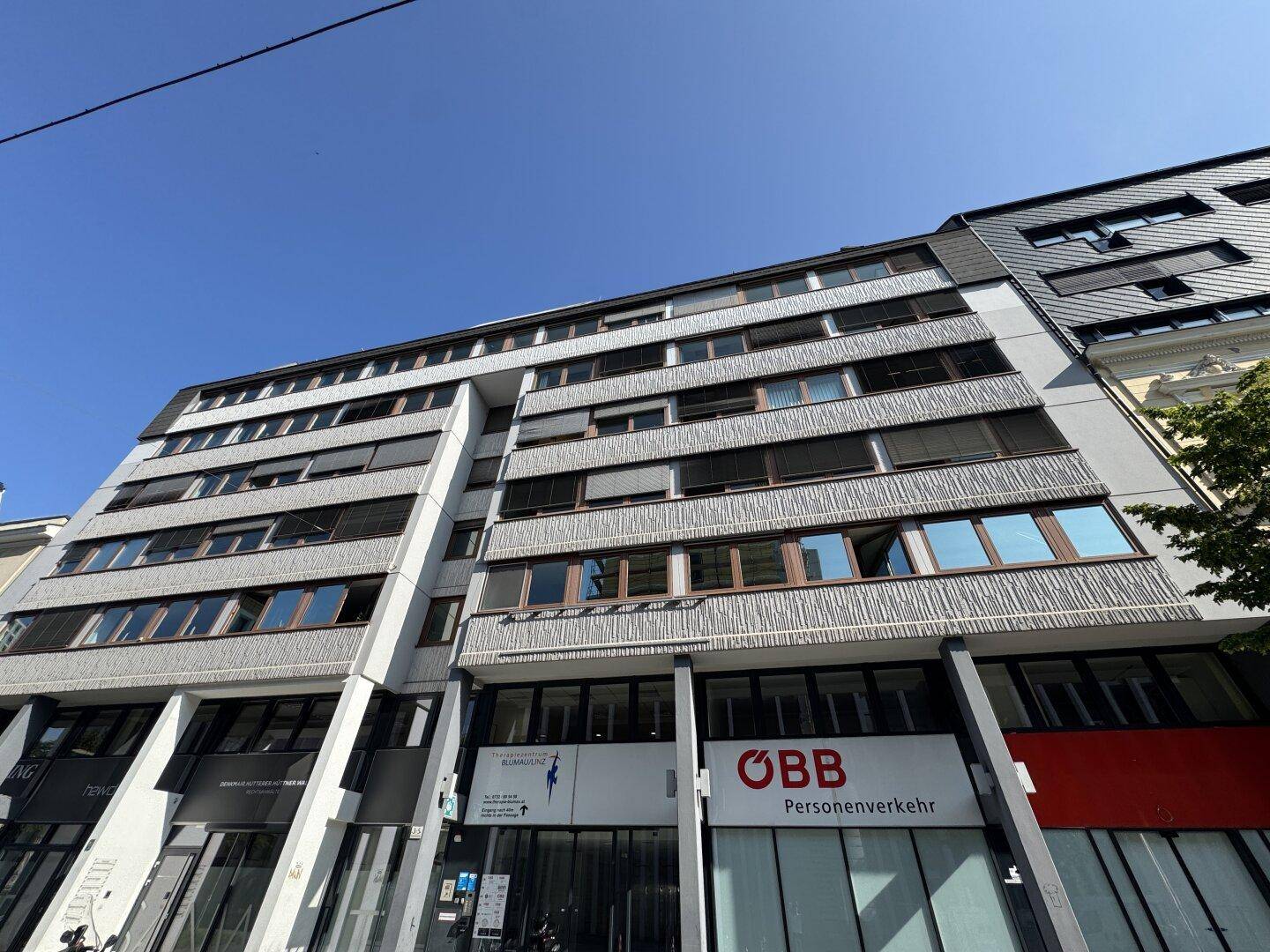 Mehrstöckiges Geschäftsgebäude mit moderner Fassade, großen Fenstern und klarem blauen Himmel.