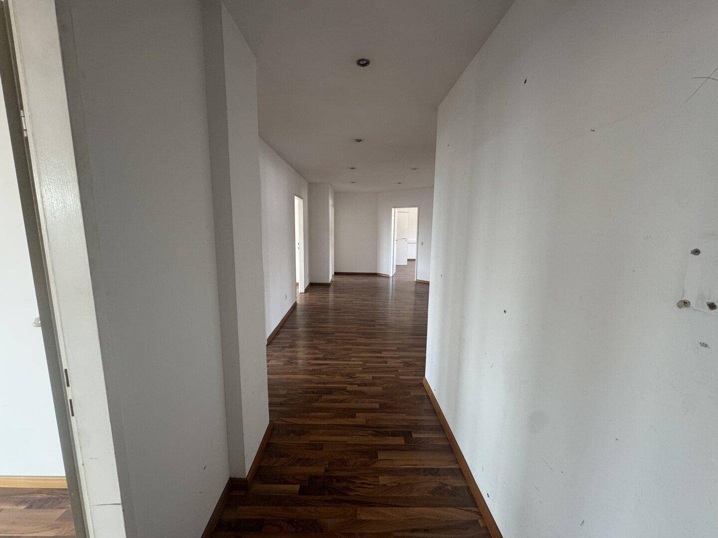 Langer, leerer Flur mit Holzboden und mehreren Türen, der zu verschiedenen Räumen führt.