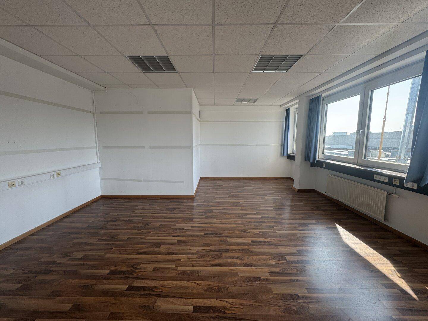 Großes, helles Büro mit Holzboden und Rasterdecke, ideal für flexible Arbeitsplatzgestaltung.