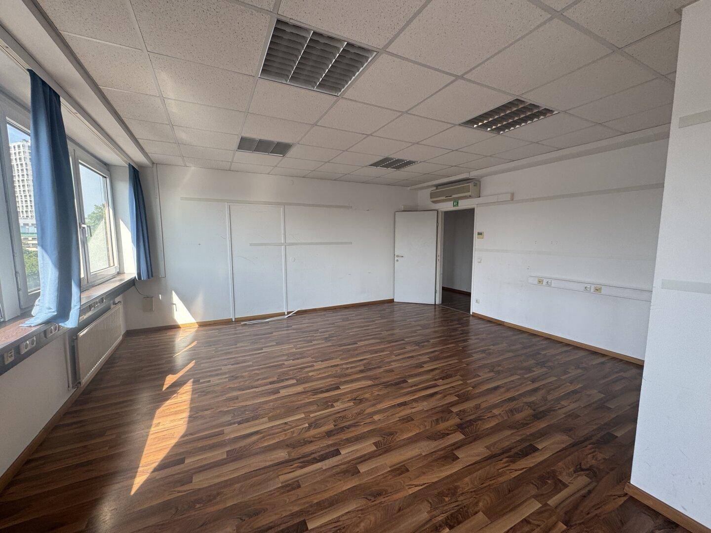 Leeres Büro mit Holzboden, Klimaanlage und Rasterdecke, bereit zur individuellen Gestaltung.