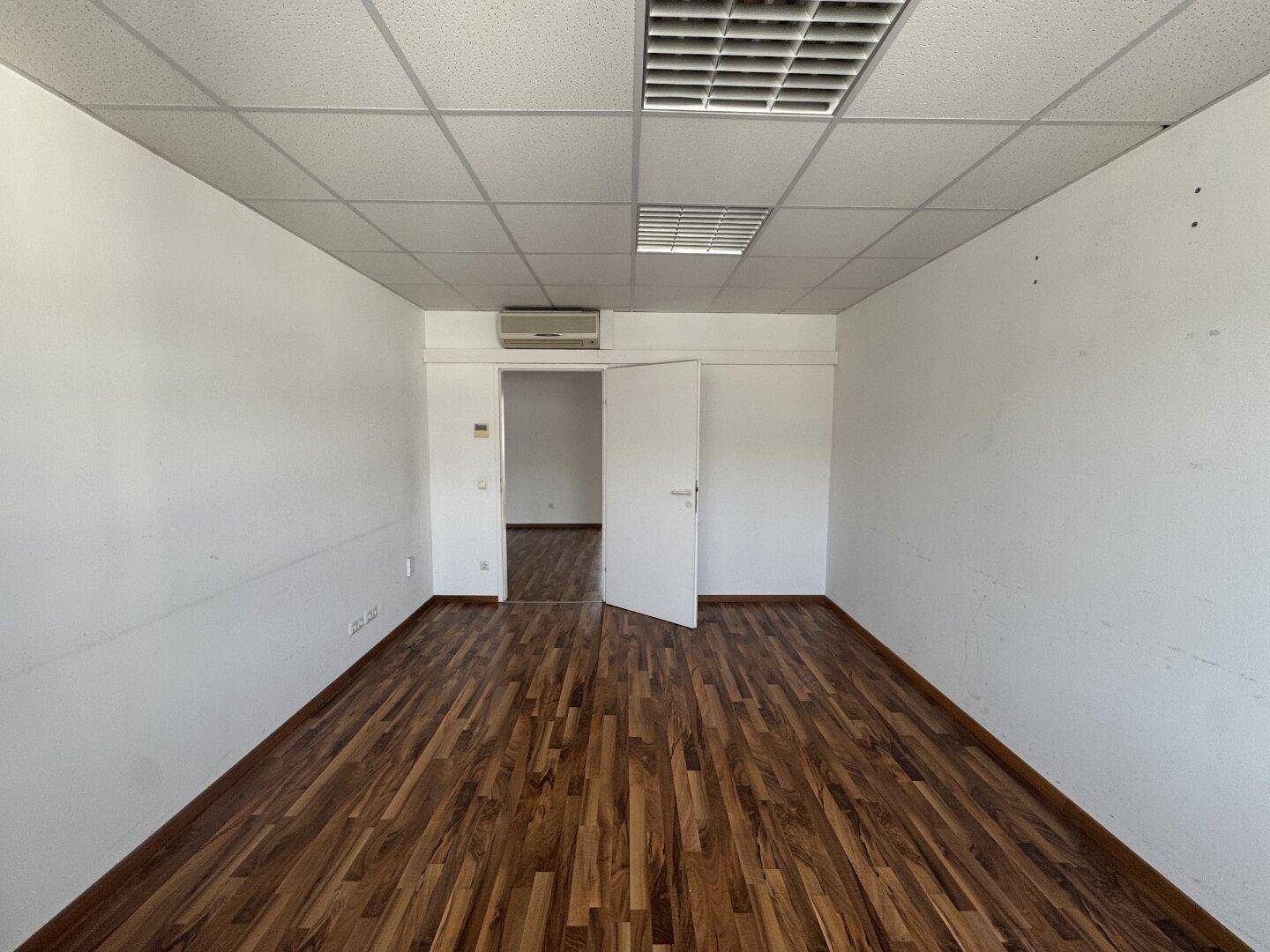 Leerer Büroraum mit Holzboden, Rasterdecke und Klimaanlage, ideal für flexible Nutzung.