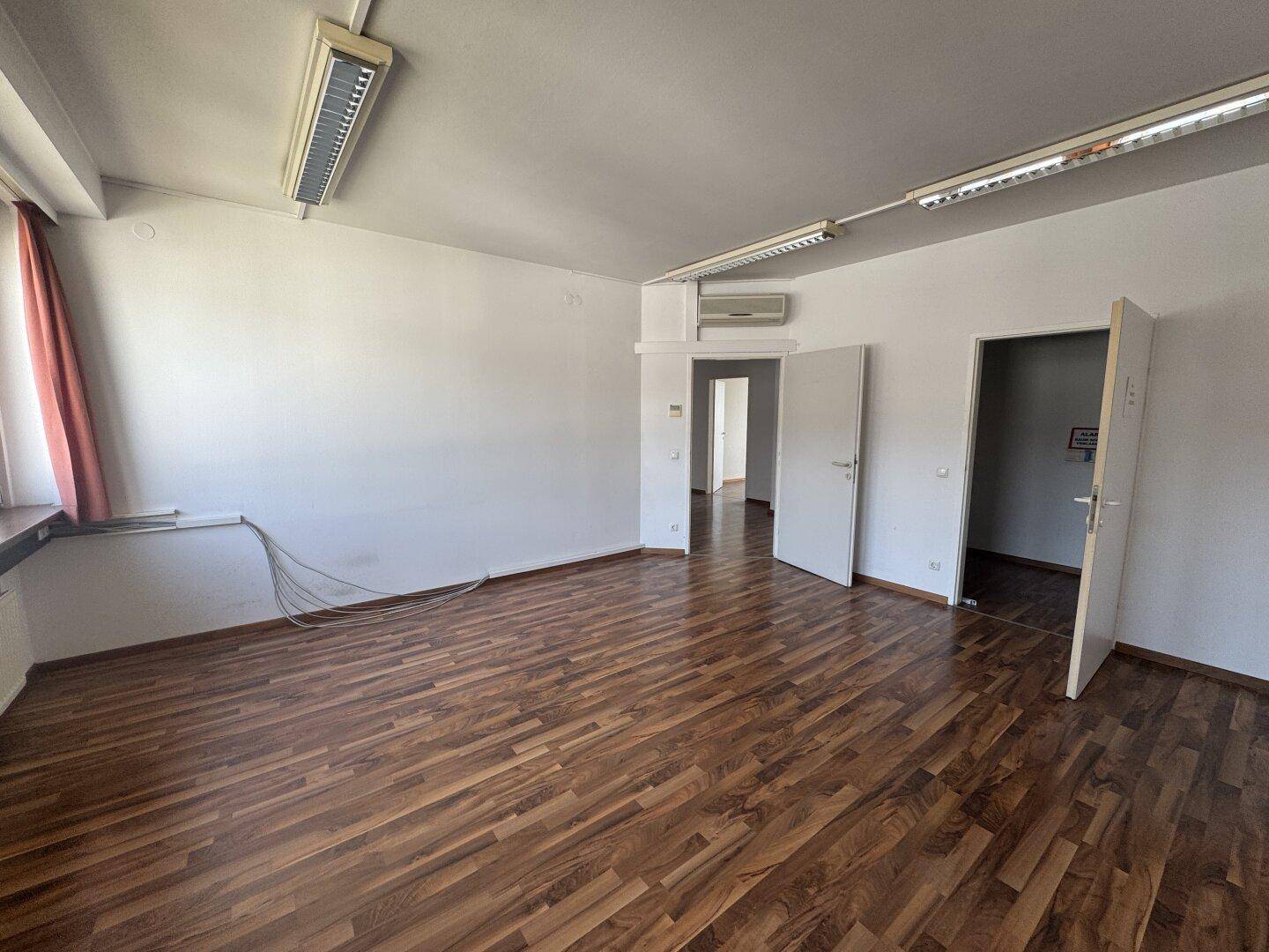 Geräumiges Büro mit Holzboden, Klimaanlage und mehreren Türen, bietet flexible Nutzungsmöglichkeiten.