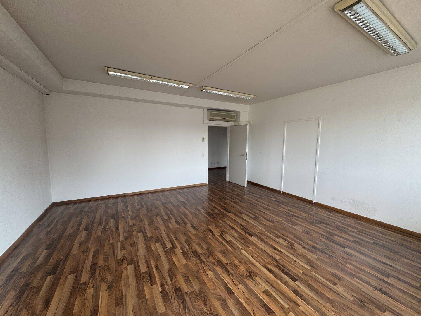 Leeres Büro mit Holzboden, Klimaanlage und Deckenbeleuchtung, bereit zur individuellen Gestaltung.