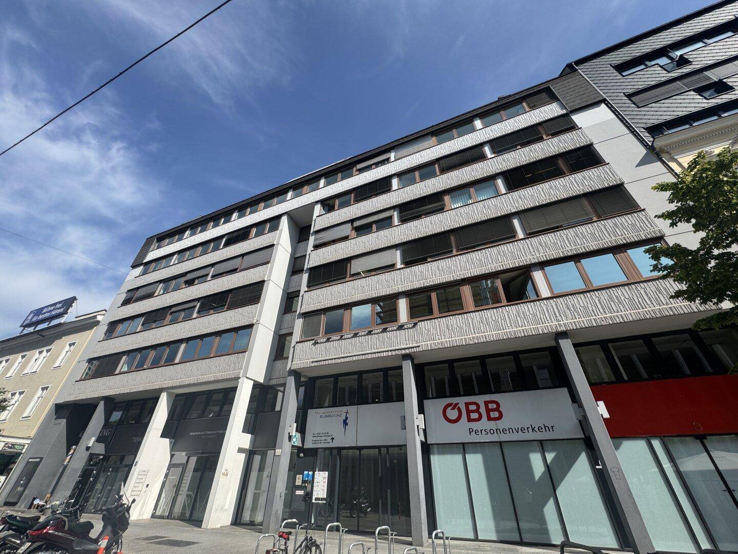 Modernes Geschäftsgebäude mit mehreren Etagen, großen Fenstern und kommerziellen Flächen im Erdgeschoss.