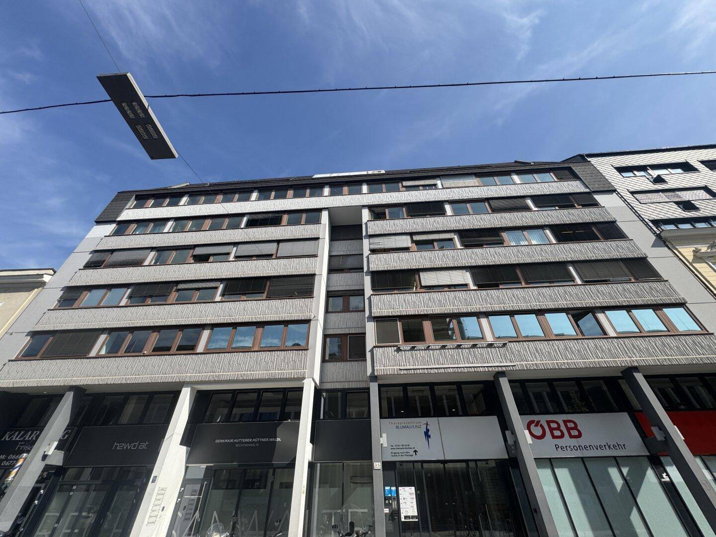 Modernes Geschäftsgebäude mit mehreren Etagen, großen Fenstern und kommerziellen Flächen im Erdgeschoss.