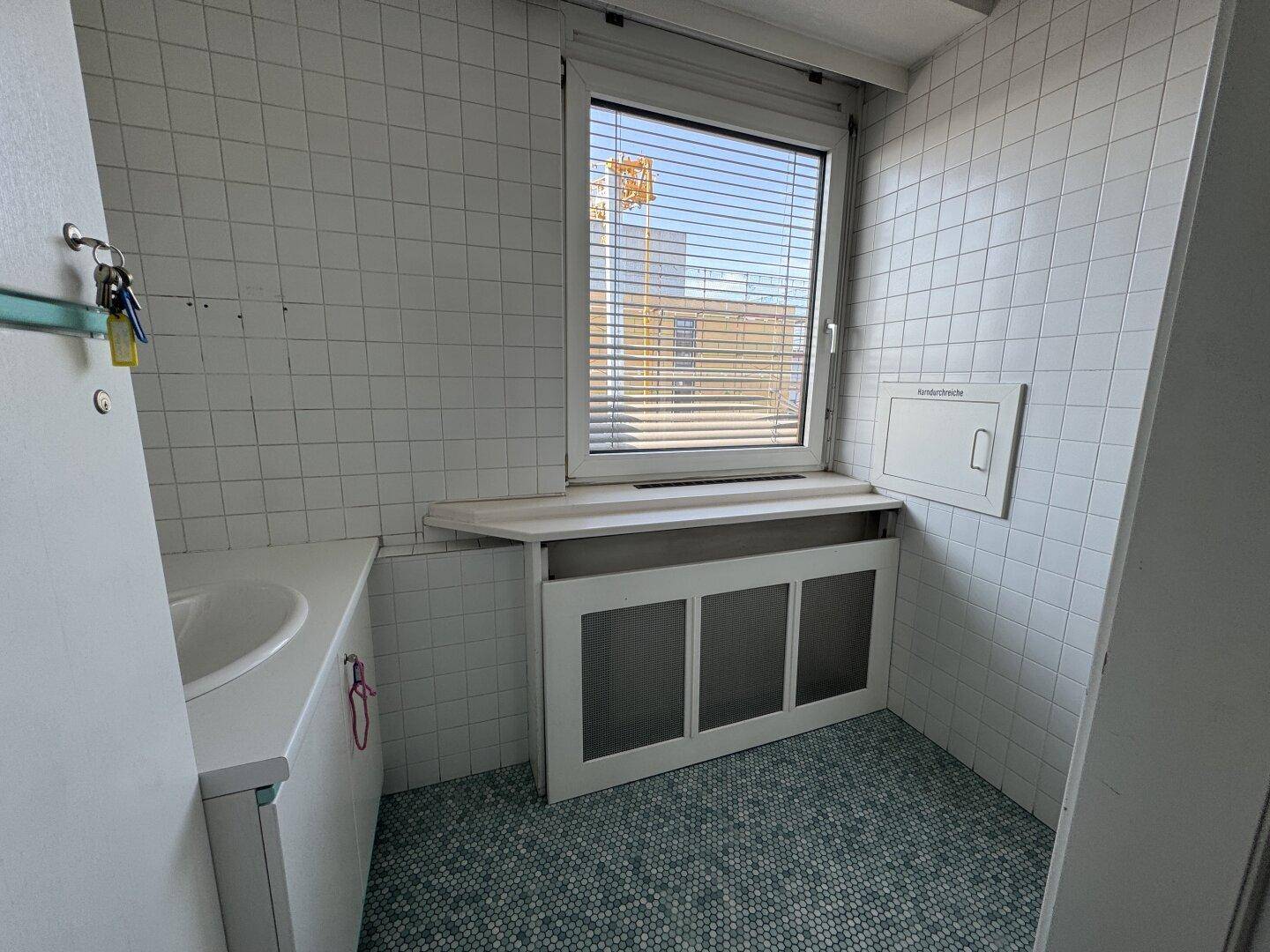 Kleines Badezimmer mit weißen Fliesen, Fenster und einem Waschbecken.