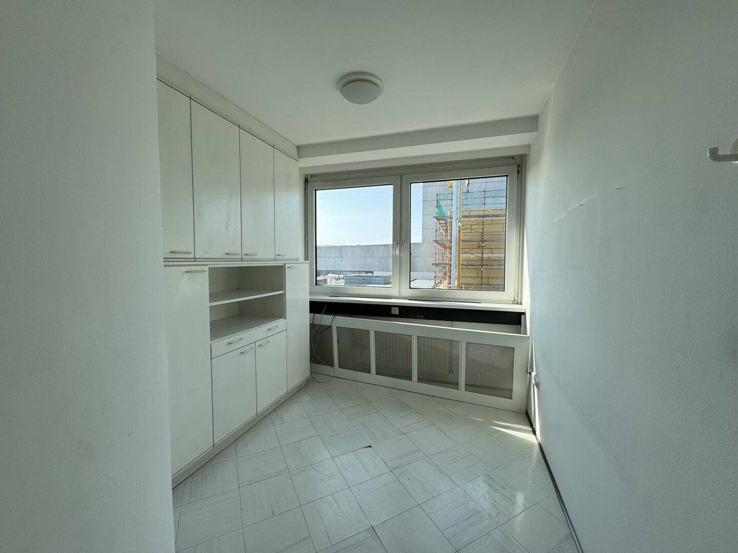 Büroraum mit weißen Einbauschränken, Fenster und Blick nach draußen.
