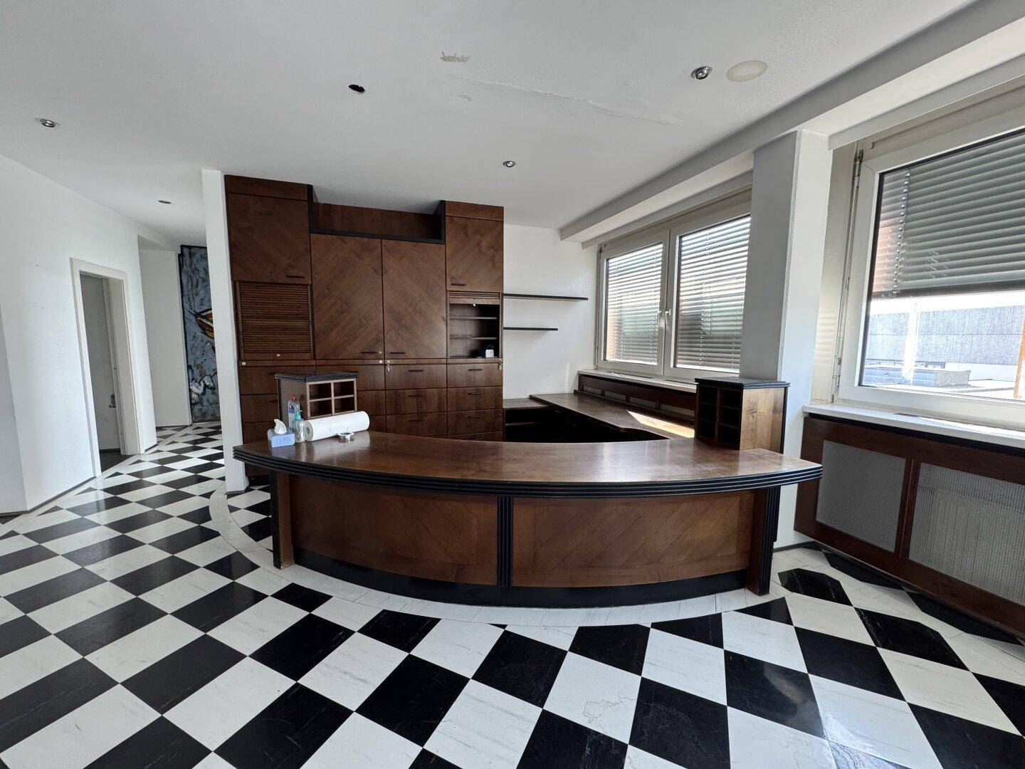 Geräumiger Büroraum mit einer eleganten Holztheke und großen Fenstern mit Jalousien.