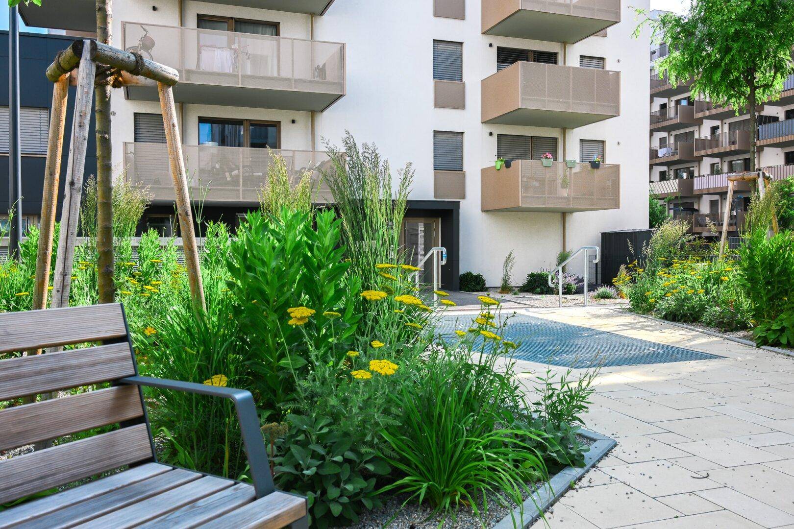 Attraktiver Außenbereich mit Sitzbank, Blumenbeeten und gepflastertem Weg vor einem modernen Wohnhaus.