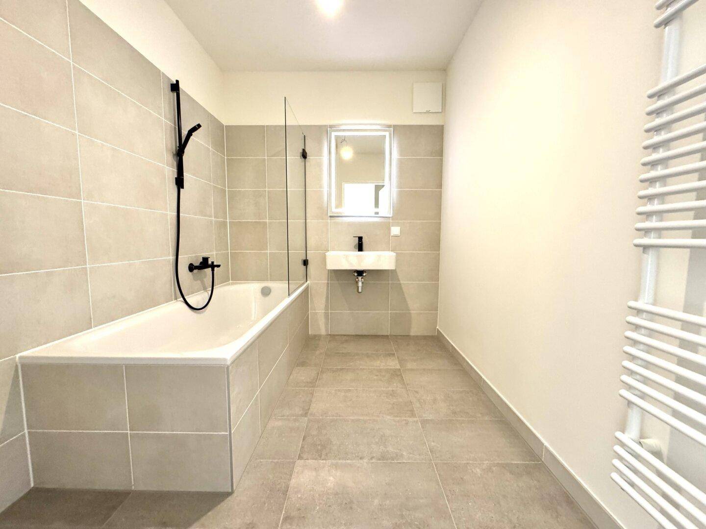 Modernes Badezimmer mit Badewanne, Einzelwaschbecken und beheiztem Handtuchhalter.