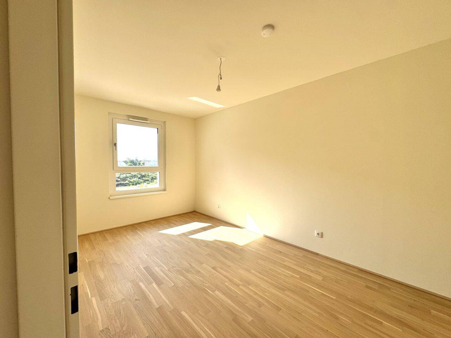 Helles Schlafzimmer mit Parkettboden und einem Fenster, das viel Tageslicht hereinlässt.