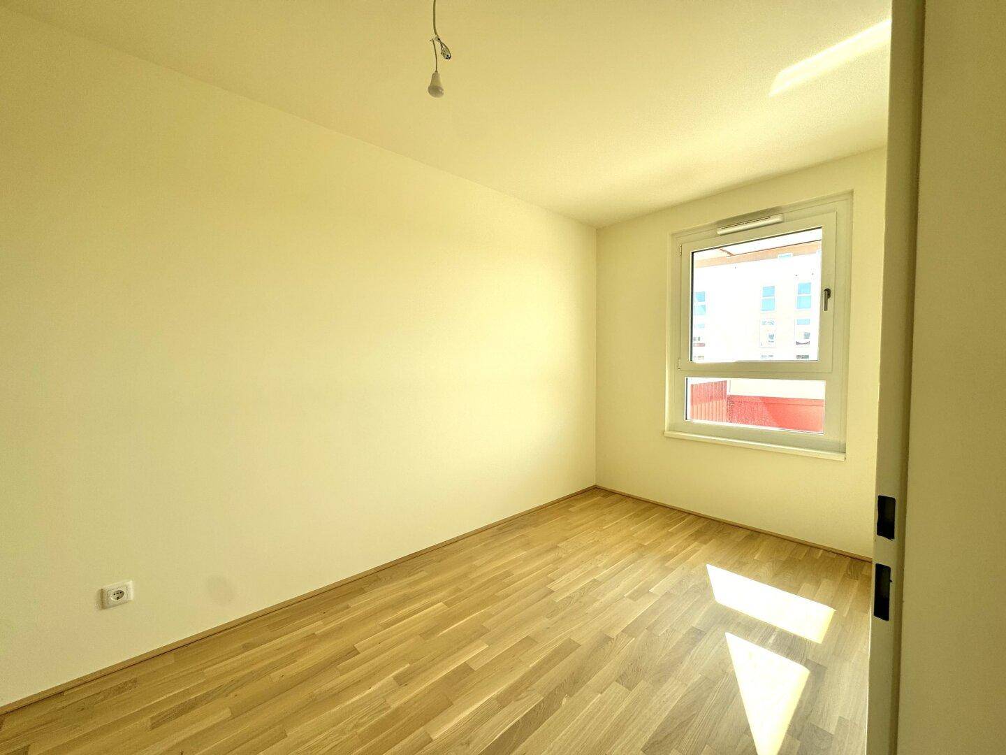 Geräumiges Schlafzimmer mit hellem Parkettboden und Blick auf die umliegenden Gebäude.